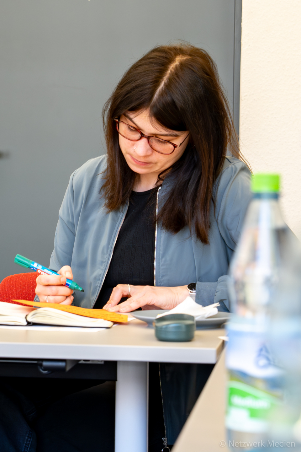 1 Frau sitzt an einem Tisch, blickt nach unten und notiert sich Arbeitsergebnisse. 