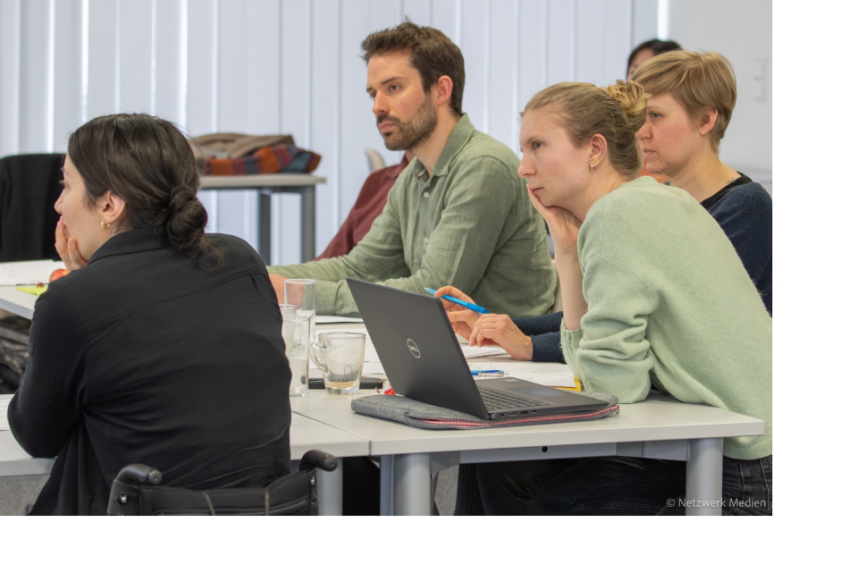3 Frauen und 1 Mann sitzen an Tischen und hören einem Redner zu. Auf dem Tisch steht ein Laptop und mehrere Gläser. 3 Frauen und 1 Mann sitzen an Tischen und hören einem Redner zu. Auf dem Tisch steht ein Laptop und mehrere Gläser.