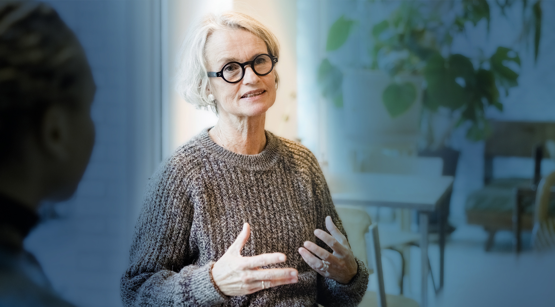 Weibliche Person mit Brille steht frontal und erläutert einen Arbeitsprozess.